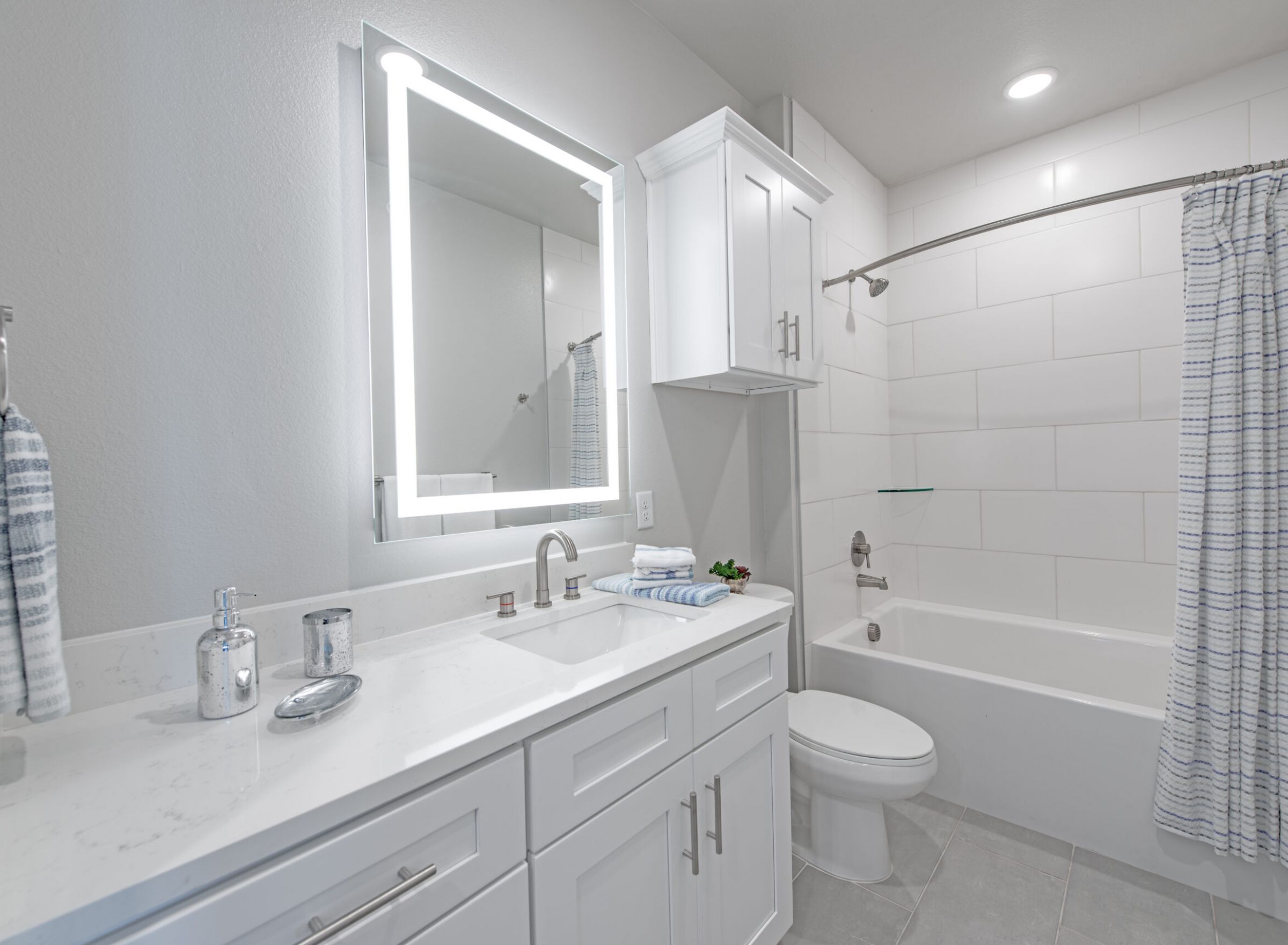 The Delta Pearland luxury apartment community bathroom with bathtub, abundant cabinet storage, and large dual vanity, his and hers sinks, and LED back-lit mirrors