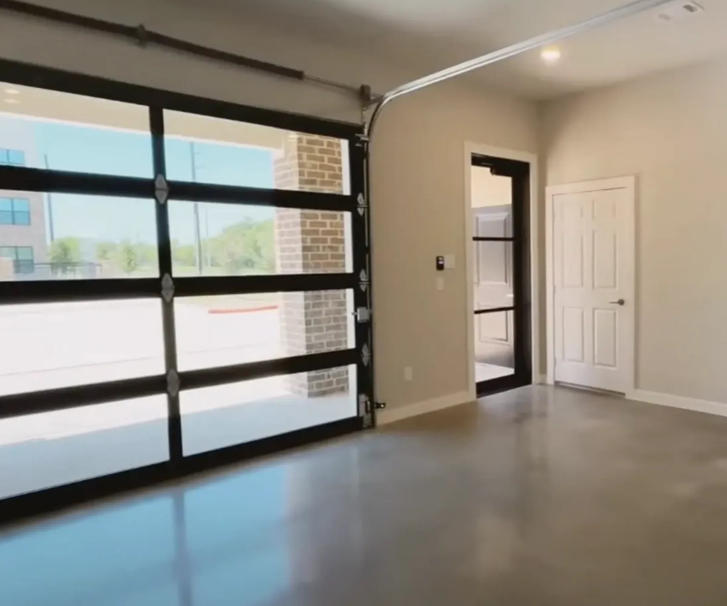 The Delta Pearland Live&Co Suites business and live spaces showing the first floor with a modern empty garage with glass-panel door, white walls, and polished concrete floor, lit by natural light.